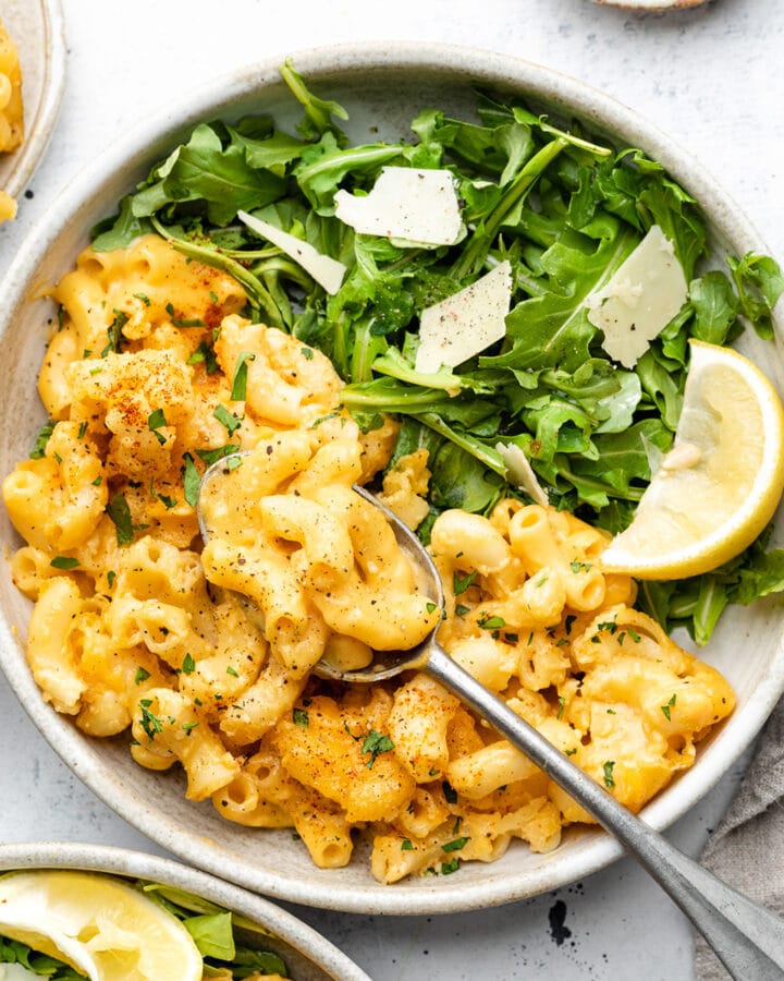 Mac and cheese in a white bowl with arugula salad.
