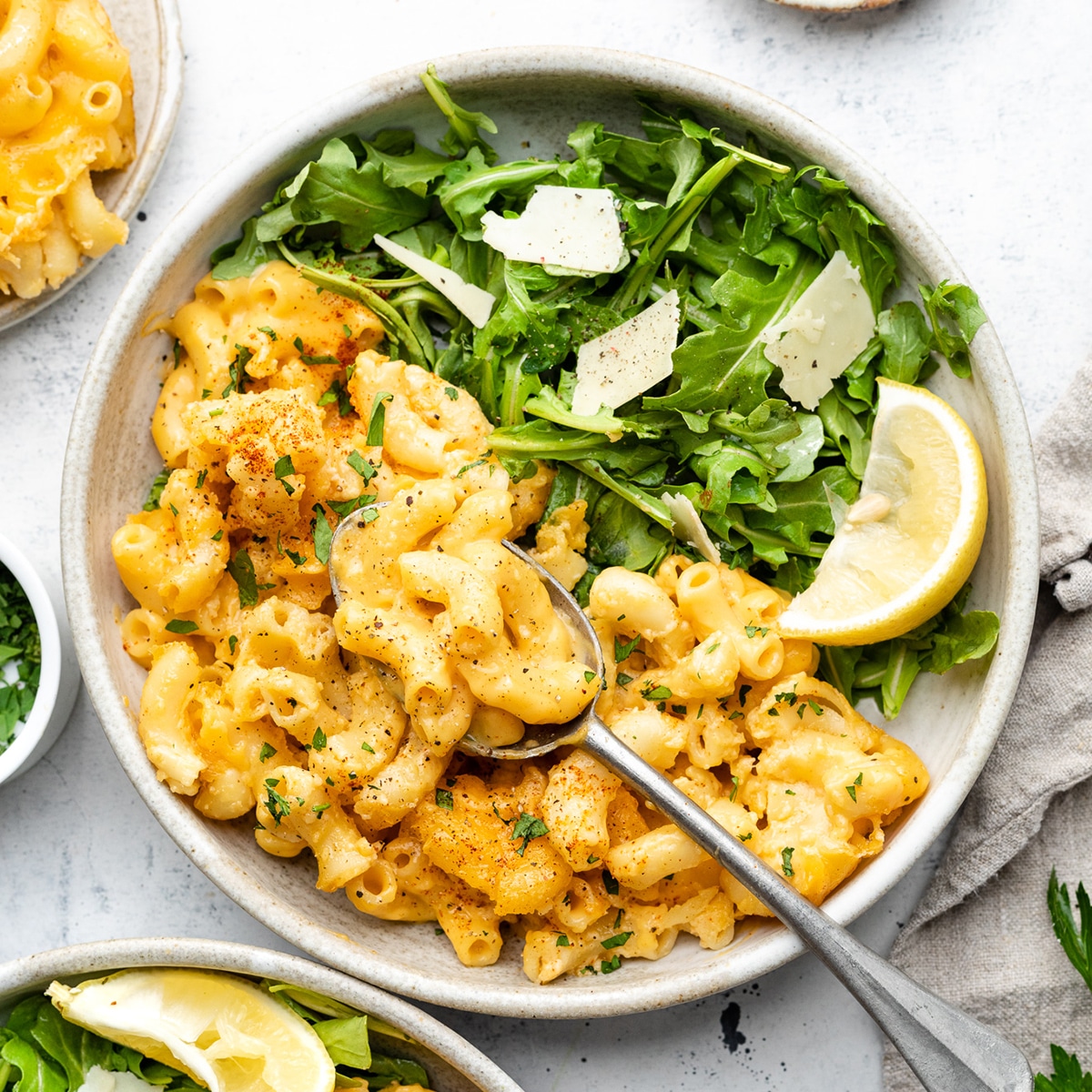 Mac and cheese in a white bowl with arugula salad.