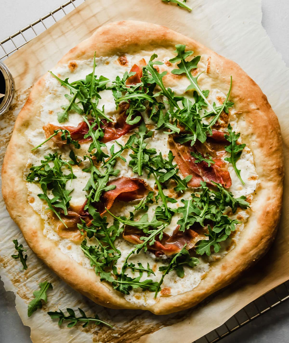 Prosciutto pizza topped with fresh arugula, sitting on a piece of parchment paper.