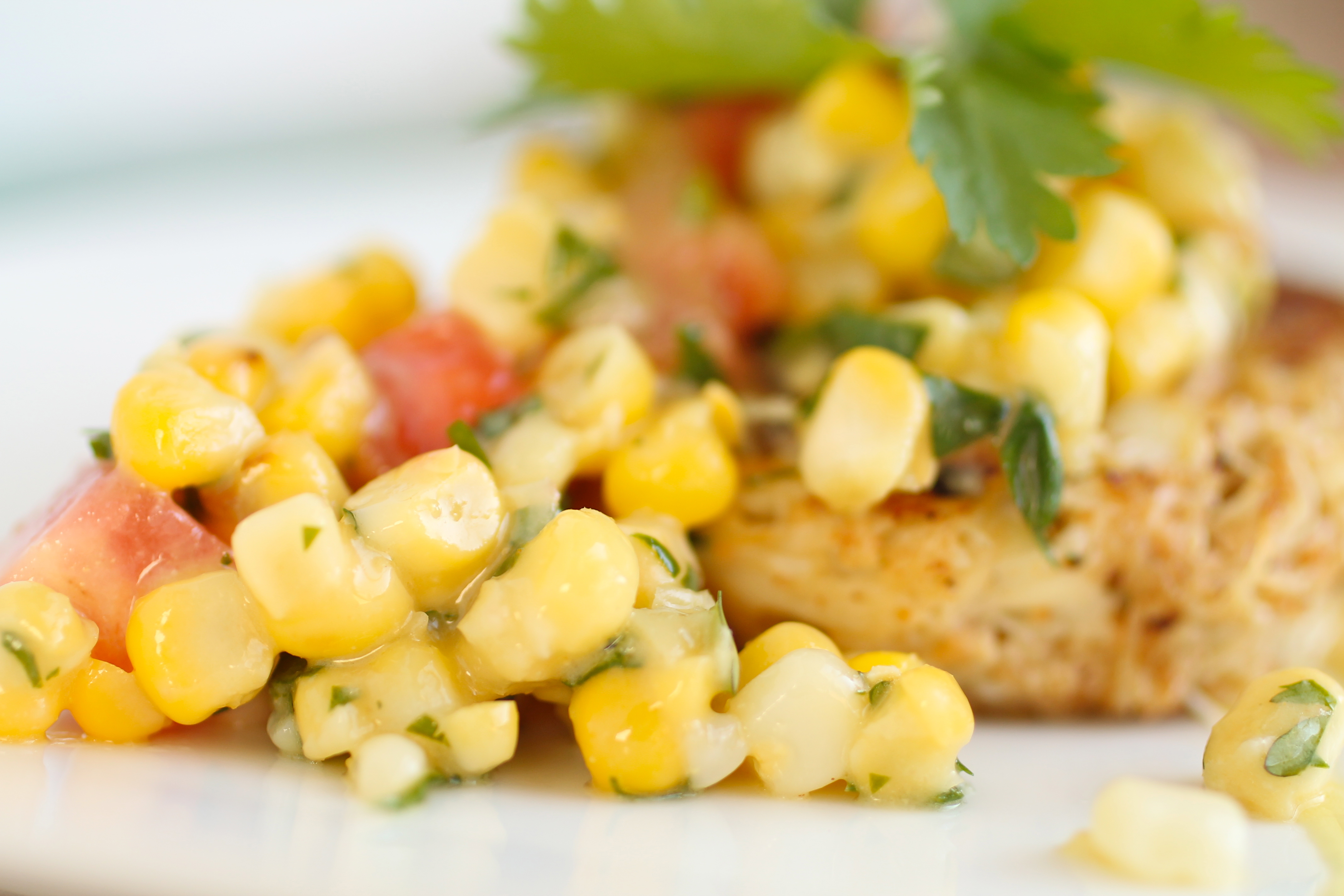 Close up of a crab cake topped with corn salsa and a sprig of fresh cilantro.
