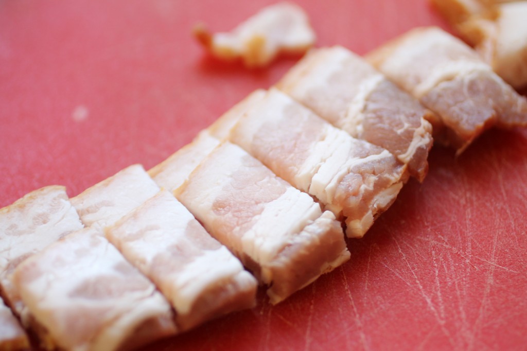Bacon strips sliced into small pieces on a red cutting board.