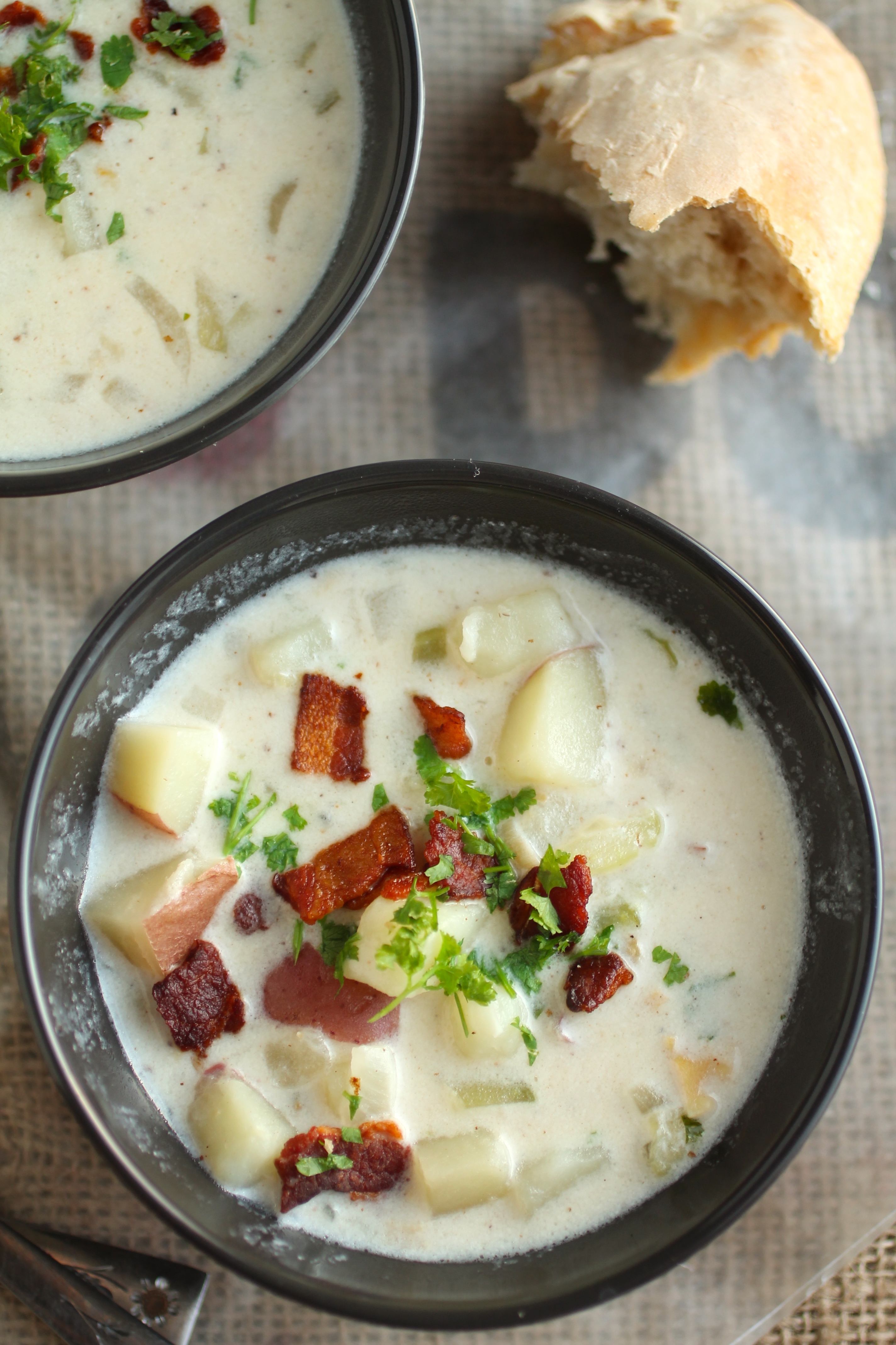 Aerial view of a black bowl filled with clam chowder, topped with crispy bacon and fresh parsley.