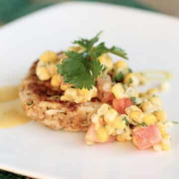 Crab cake topped with corn salsa and a sprig of fresh cilantro.