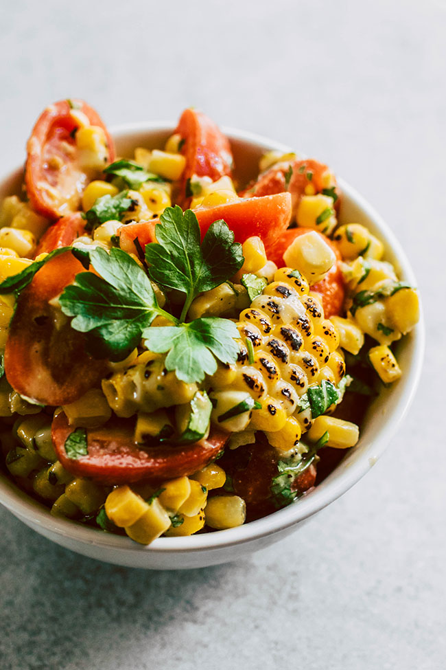 Grilled corn salsa in a white bowl, topped with a sprig of fresh cilantro.