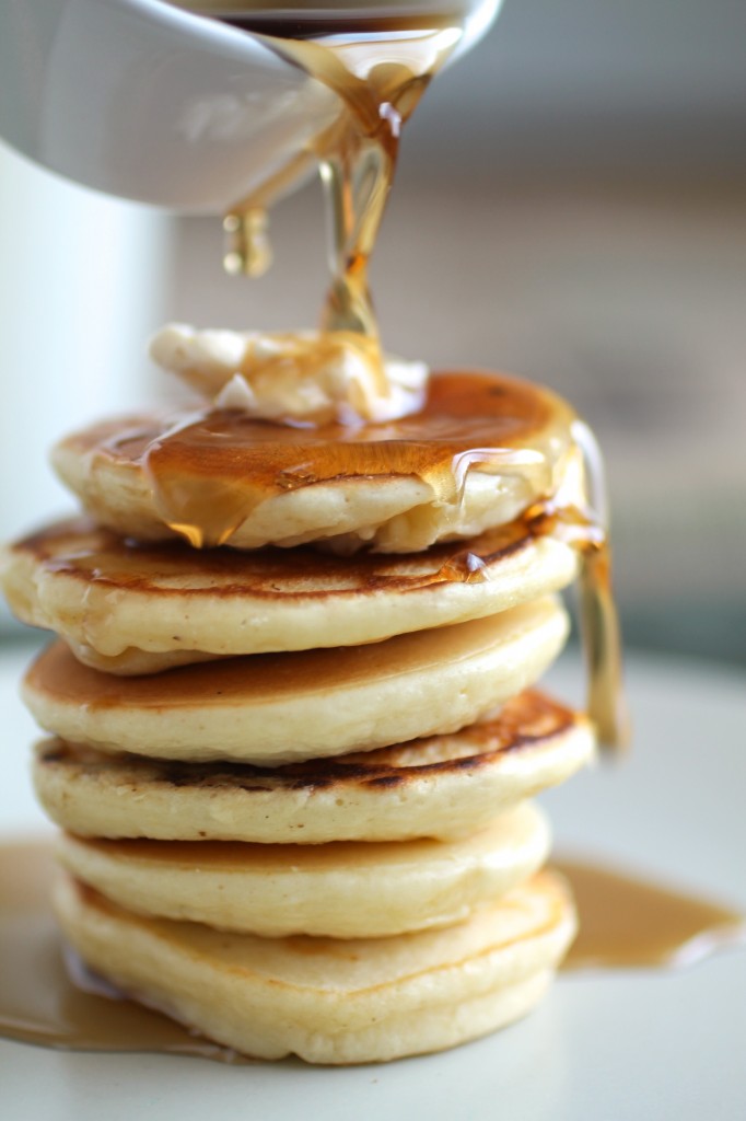 White dish pouring maple syrup over a stack of pancakes.