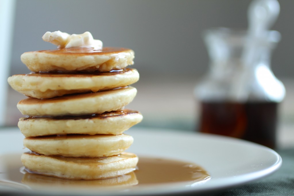 Close up of a pool of maple syrup on the plate next to a stack of pancakes.