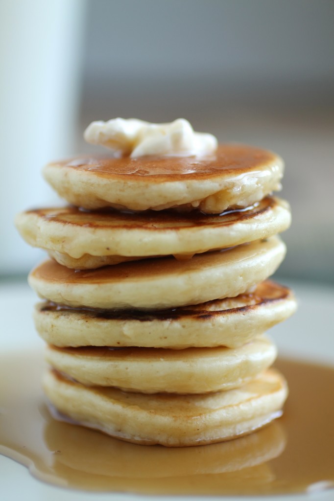 Stack of pancakes topped with a pat of butter, with maple syrup running down the sides.