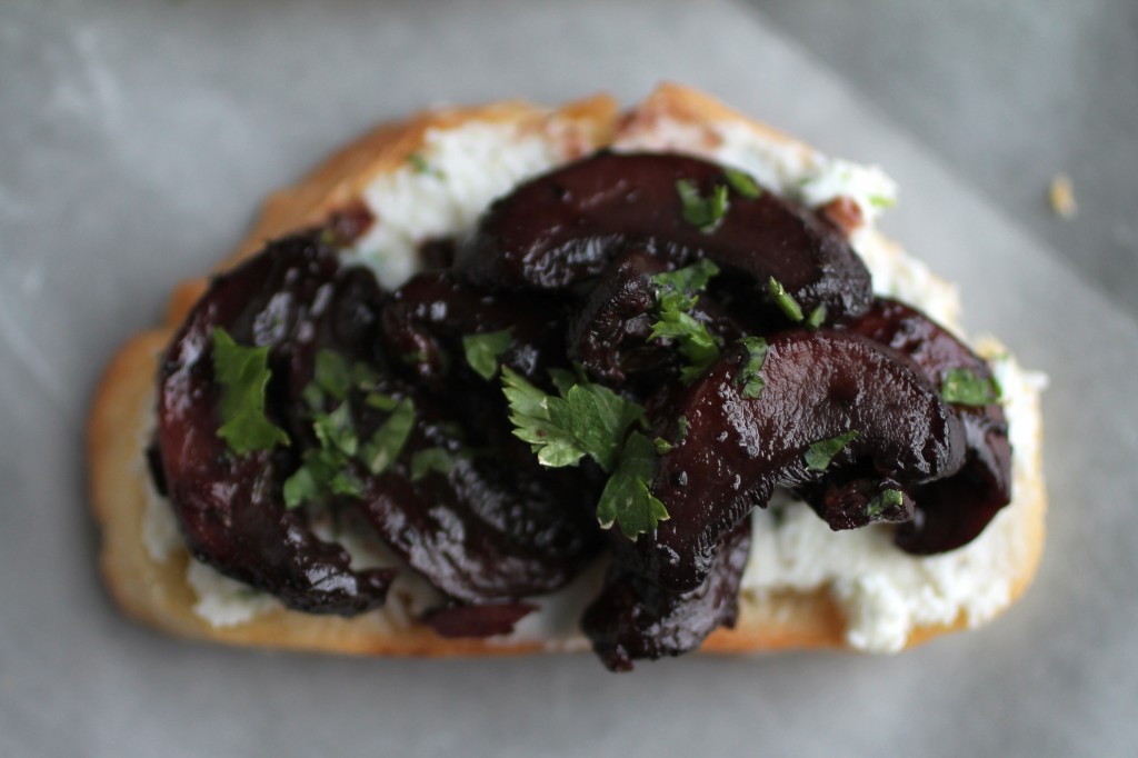 Close up of roasted mushrooms on top of a piece of crostini, topped with fresh parsley.