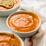 Three small white bowls filled with creamy tomato soup.