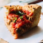 Slice of deep dish pizza topped with fresh basil.