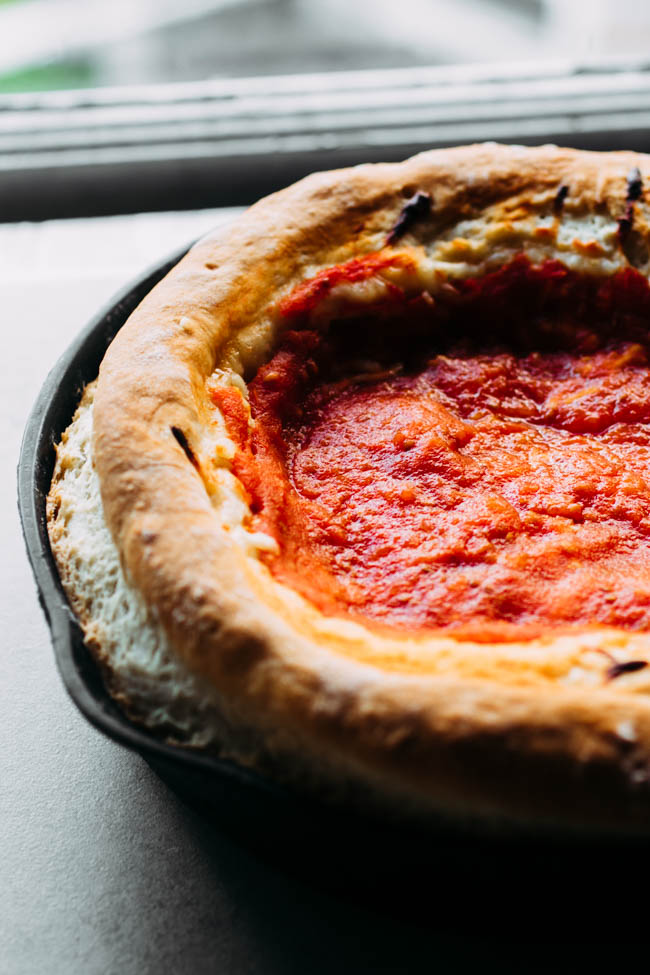 Deep dish pizza topped with tomato sauce in a cast iron skillet.