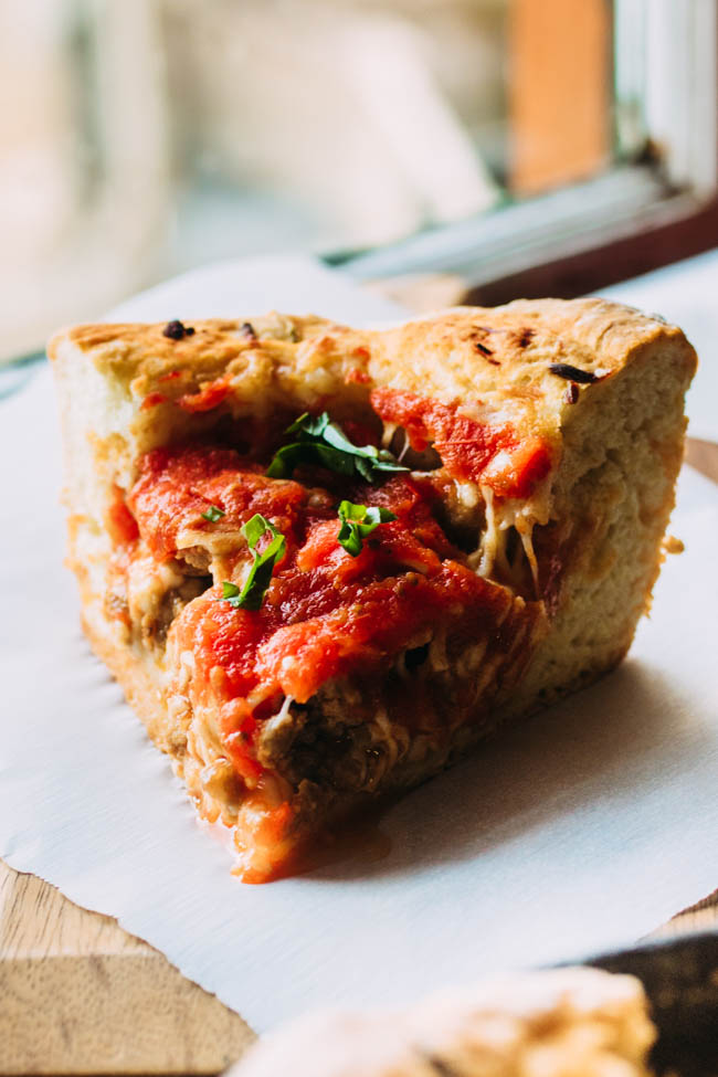 Slice of deep dish pizza on a piece of white parchment paper in front of a window.