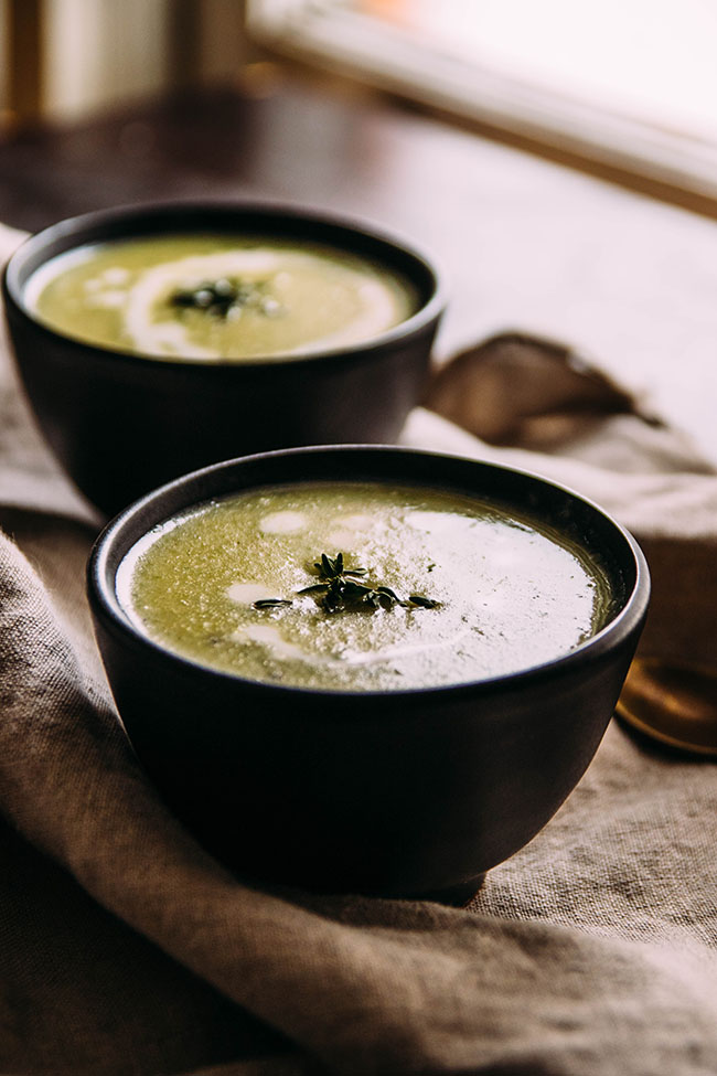Green soup in small black bowls on a brown background.