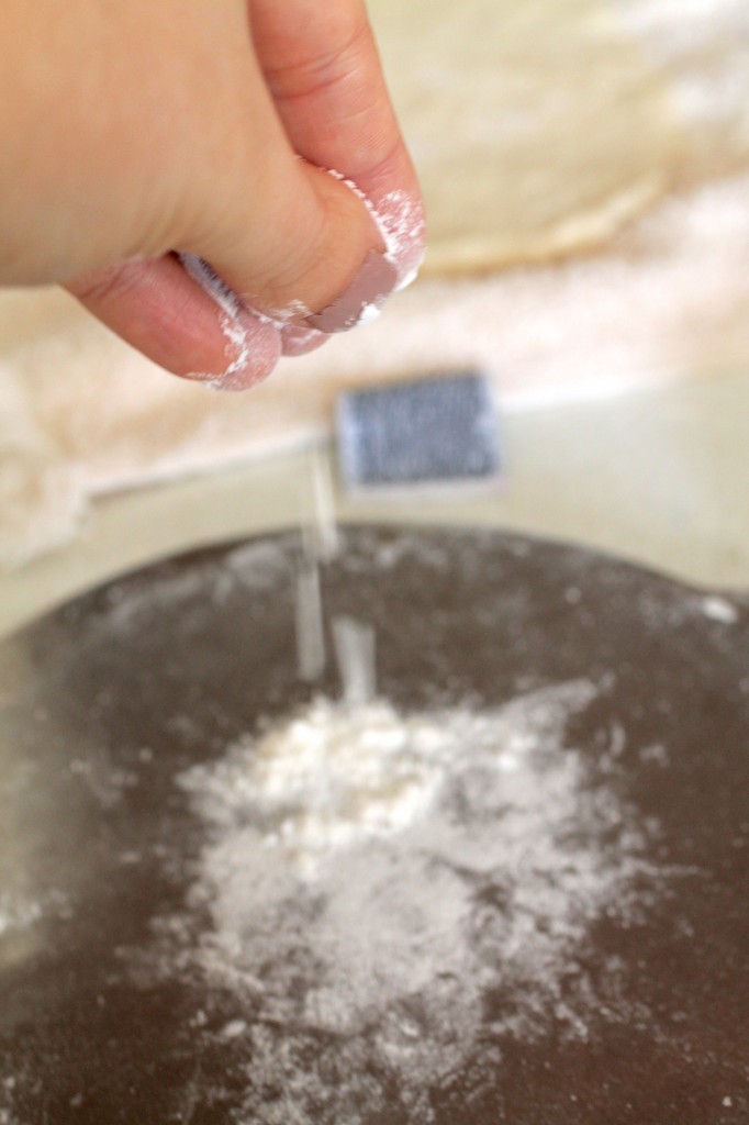 Woman\'s hand sprinkling flour onto a tortilla press.
