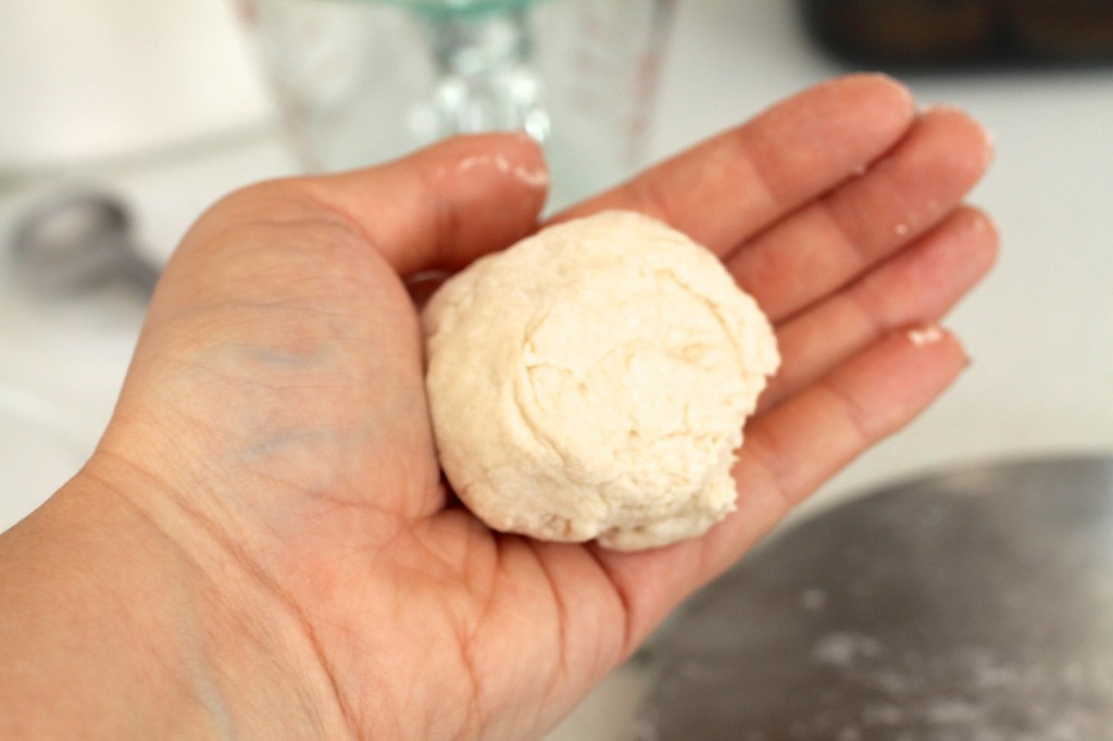 Woman\'s hand holding a piece of flour tortilla dough that fits in the palm of her hand.