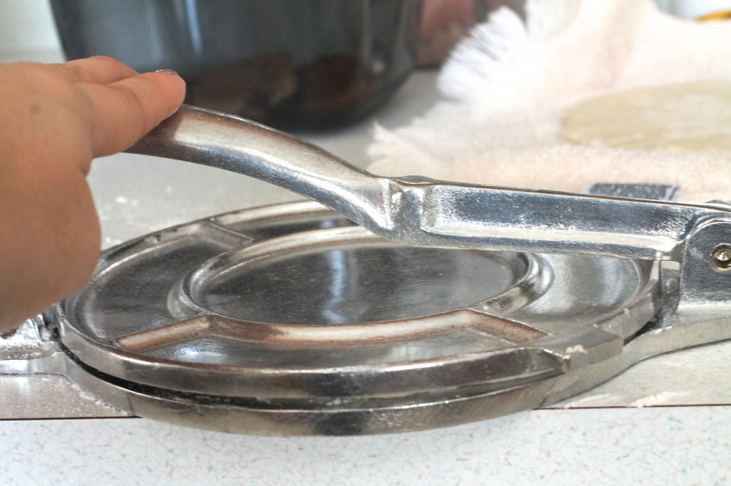 Woman\'s hand pressing a tortilla with a silver tortilla press.