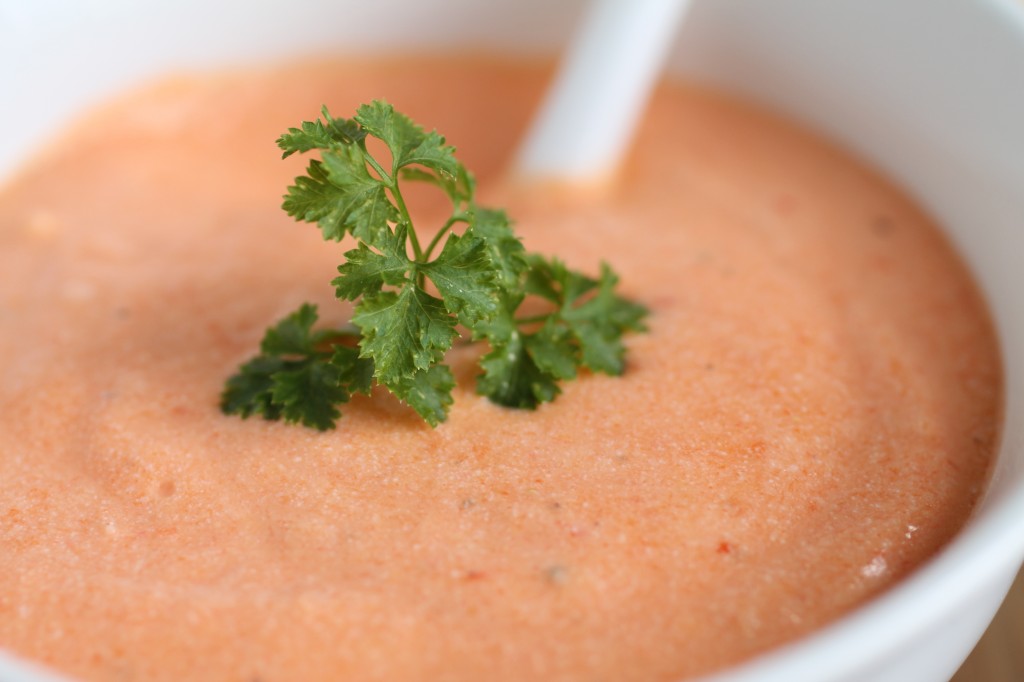 Close up of red pepper dip, topped with a sprig of fresh parsley.