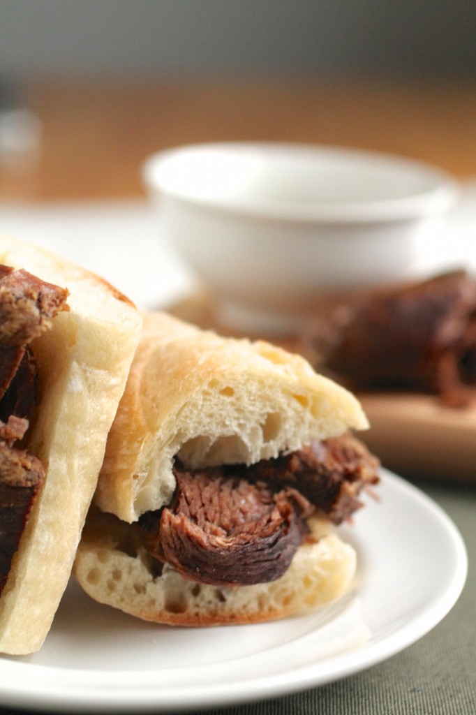 Two halves of a french dip sandwich next to a small white bowl.