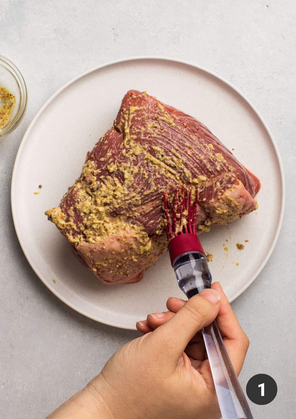 Brushing mustard onto beef roast with a pastry brush.