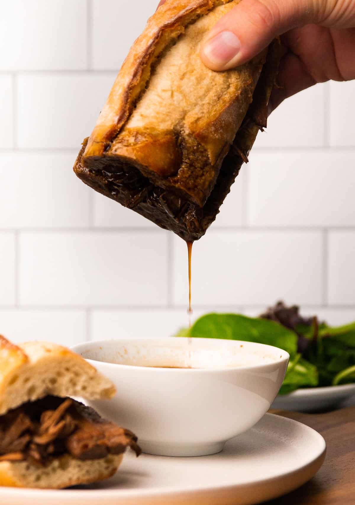 Dipping a french dip into a bowl of au jus.