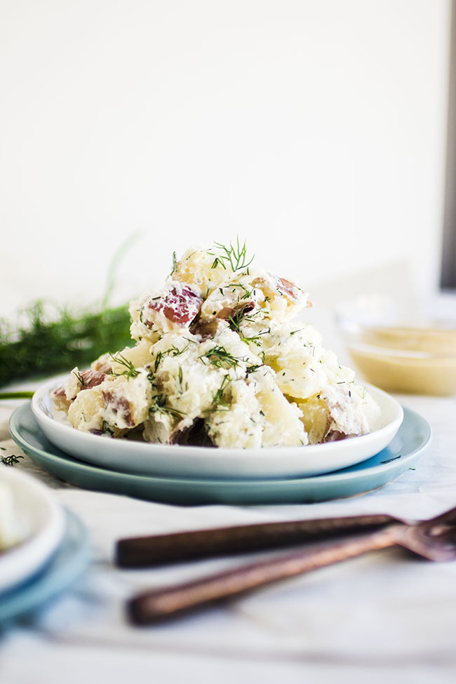 Potato salad on a stack of blue and white plates.