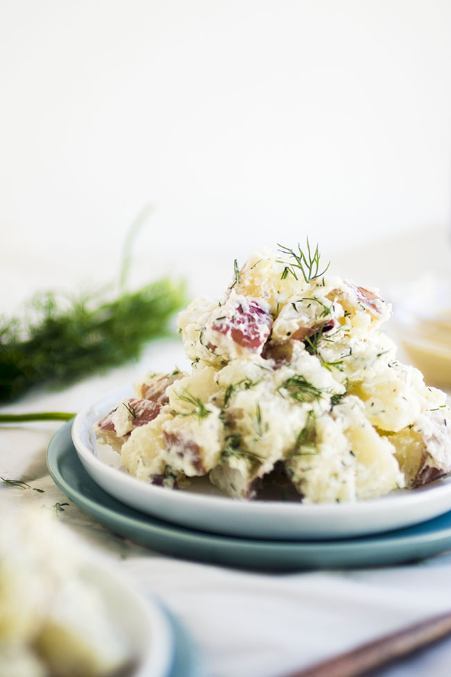 Potato salad on a white plate, topped with fresh dill.
