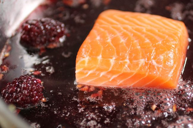 Raw salmon in a skillet with blackberry sauce.