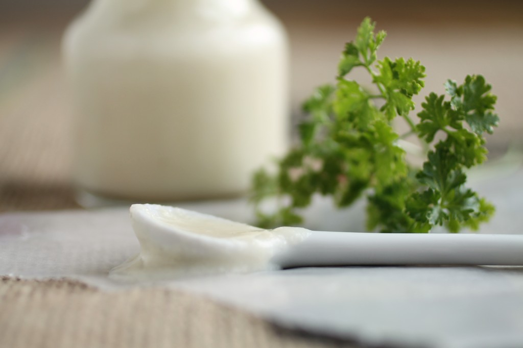 White spoon covered in alfredo sauce next to a sprig of fresh parsley.