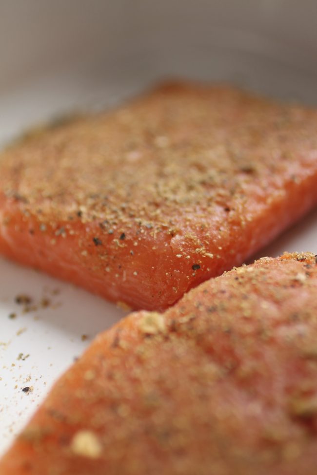 Raw salmon topped with a spice rub in a white baking dish.