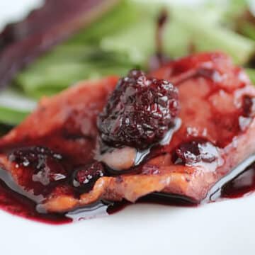 Salmon topped with blackberry sauce on a white plate.