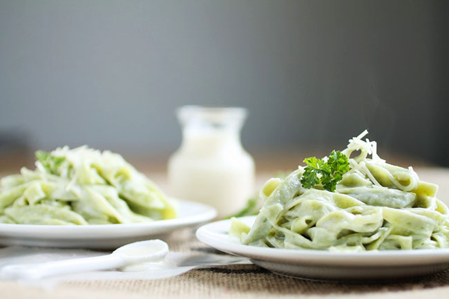 Two white plates filled with spinach fettuccine and topped with fresh parsley.