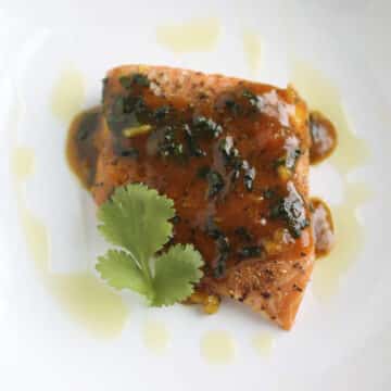 Salmon with orange sauce, topped with a sprig of fresh cilantro.