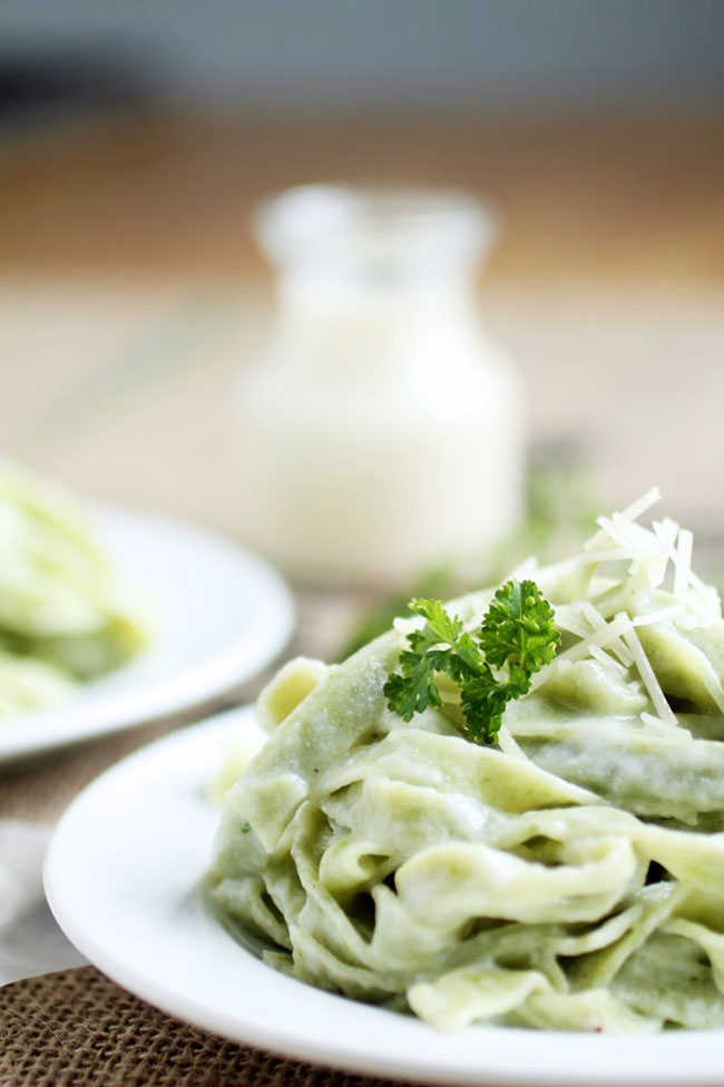 Spinach fettuccine on a white plate in front of a glass jar of alfredo sauce.