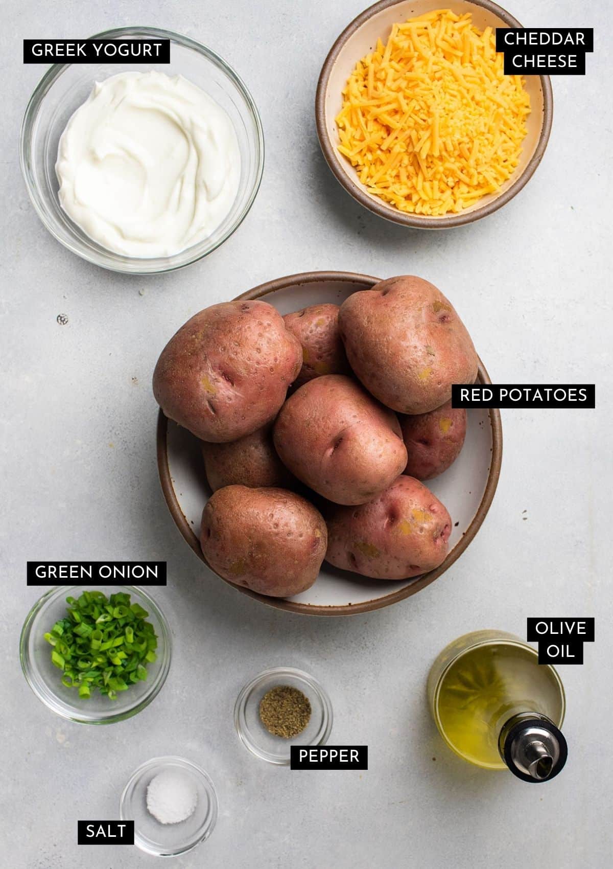 Red potatoes, greek yogurt, cheddar cheese, and seasonings on a white table.