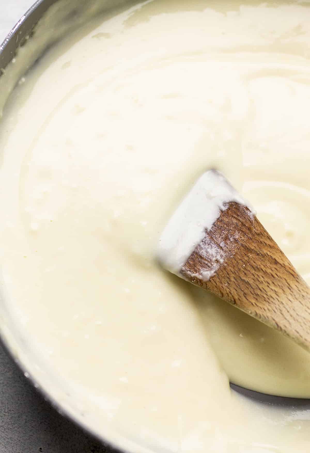 Wooden spoon stirring white sauce in a skillet.
