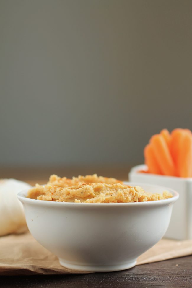 Garlic hummus in a white bowl next to a dish of baby carrots.