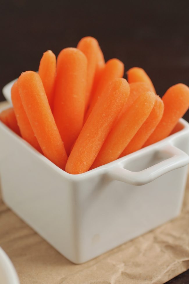 Baby carrots in a square white dish.