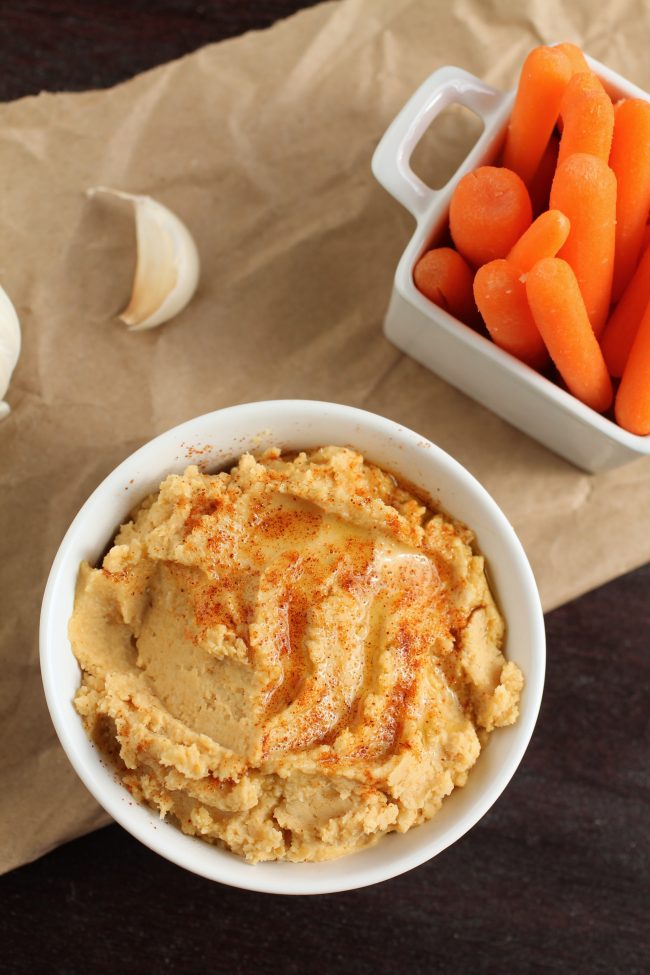 Hummus in a white bowl next to a dish full of carrots.