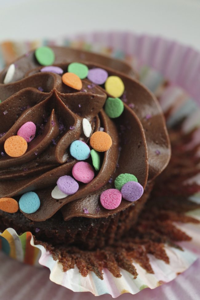 Striped wrapper peeling off a chocolate cupcake with frosting and sprinkles.