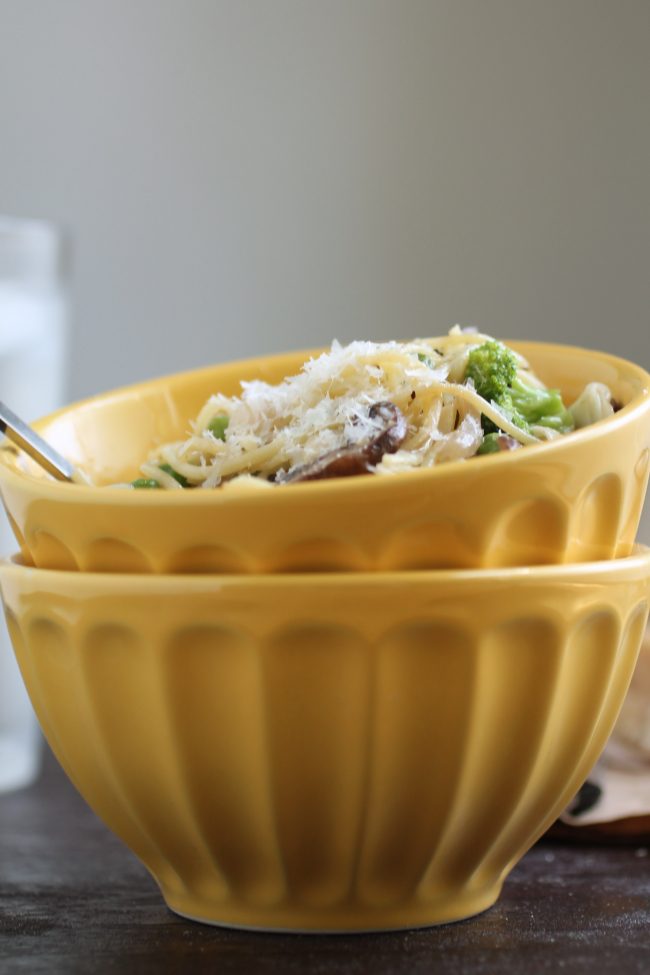 Two yellow bowls stacked in a pile with spaghetti and vegetables in the top bowl.