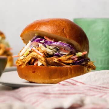 BBQ chicken sandwich with coleslaw on a white plate.