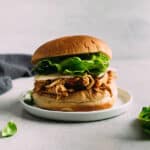 Shredded barbecue chicken on a sandwich roll with cheese and lettuce.