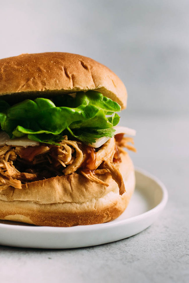 Barbecue chicken on a sandwich roll with cheese and lettuce.