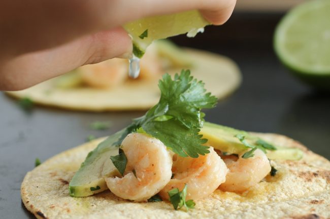 Hand squeezing lime juice onto a shrimp taco.