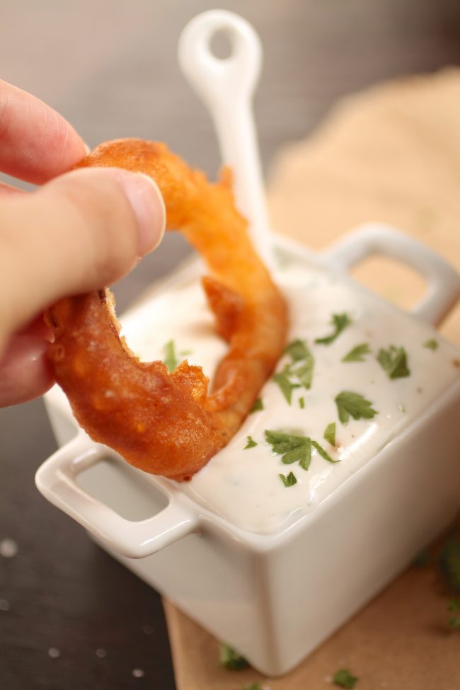 Hand dipping an onion ring into a dish of sauce.