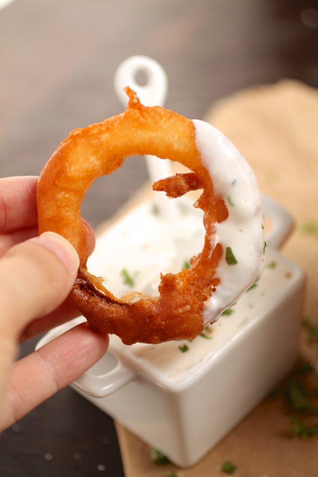 Hand holding an onion ring with yogurt sauce covering one side.