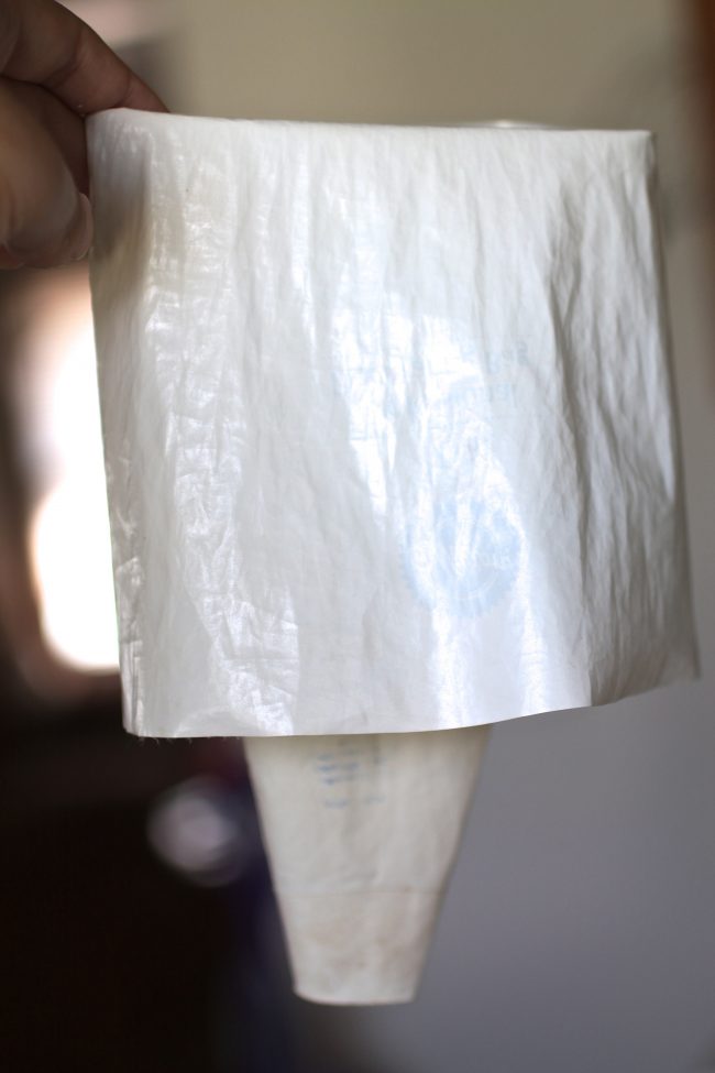 Hand holding a white pastry bag, with the top third of the bag folded down to make it easier to fill.