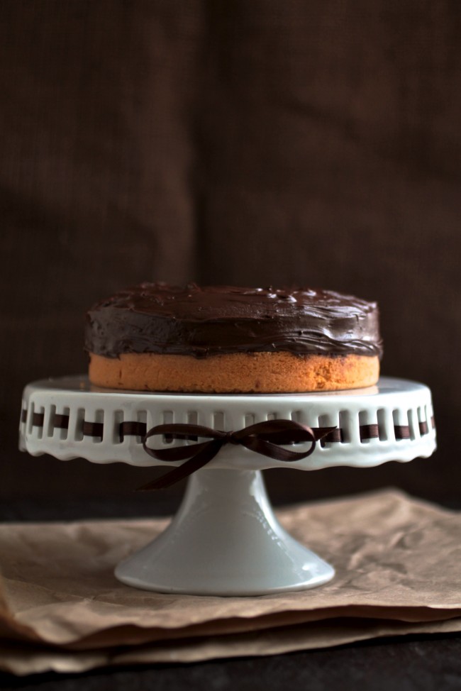 Butterscotch cake with chocolate ganache sitting on a white cake plate.