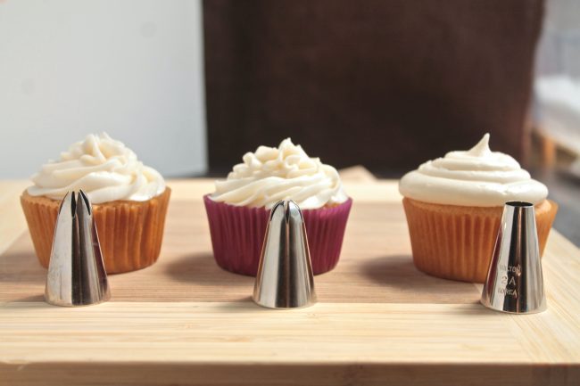 Three frosting tips, each sitting in front of a cupcake they have frosted to show the difference in texture.