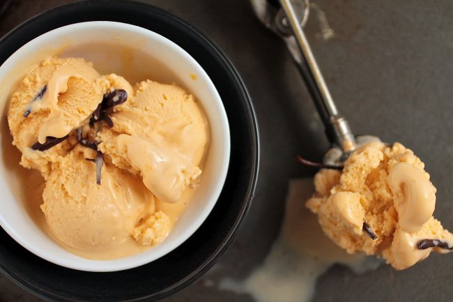 Butterscotch ice cream in a white bowl next to a silver ice cream scoop.